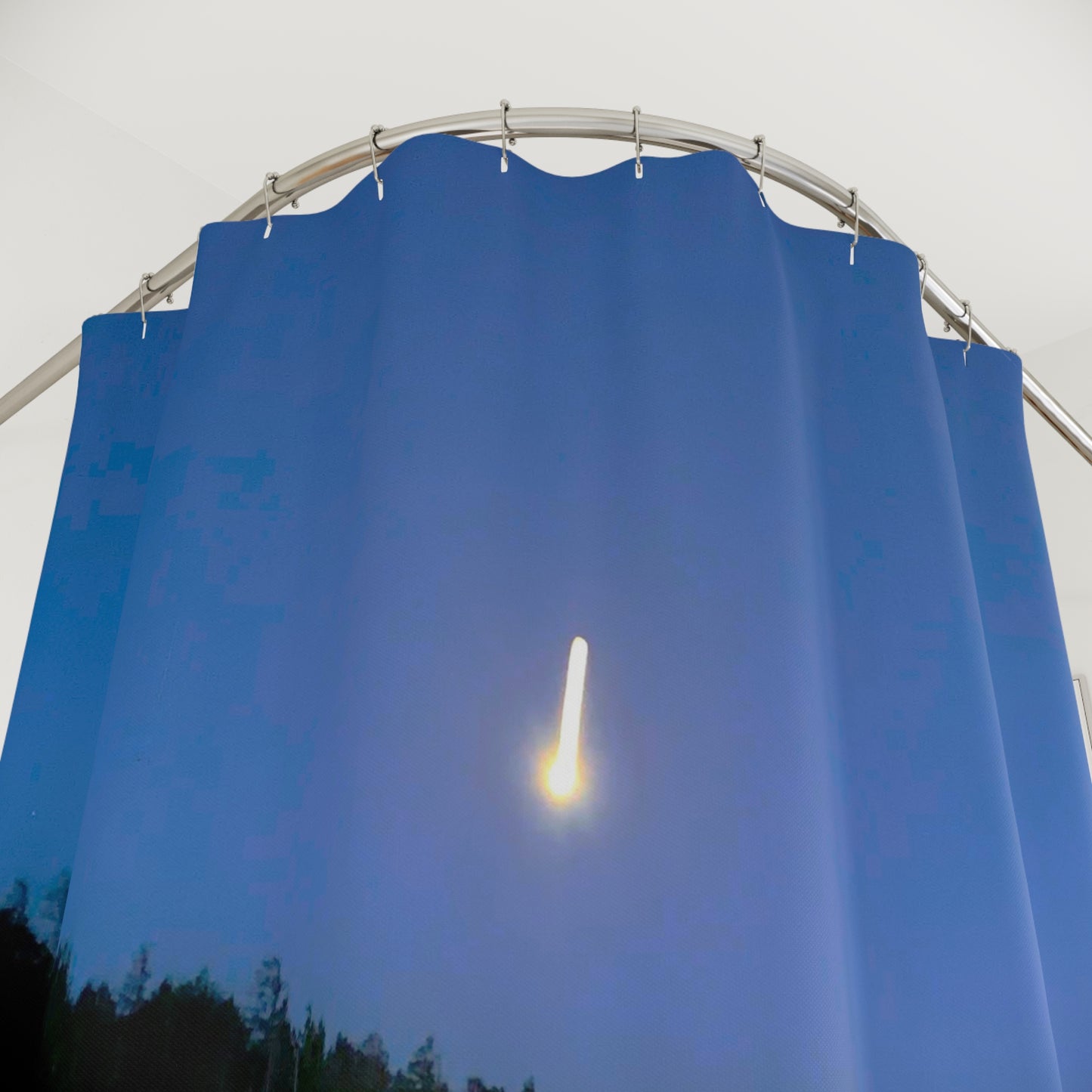 Close-up of a shower curtain showing a glowing shooting star streaking across a deep blue night sky above silhouetted treetops.