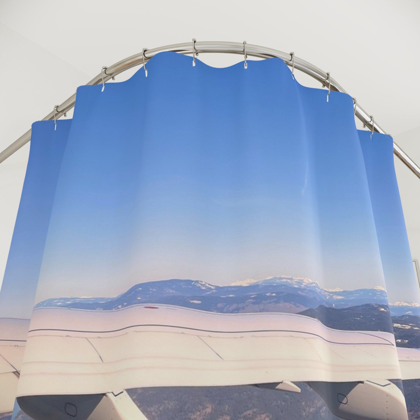 Aerial view of airplane wing flying above snow-capped mountains under a vast, clear blue sky with horizon in the distance.