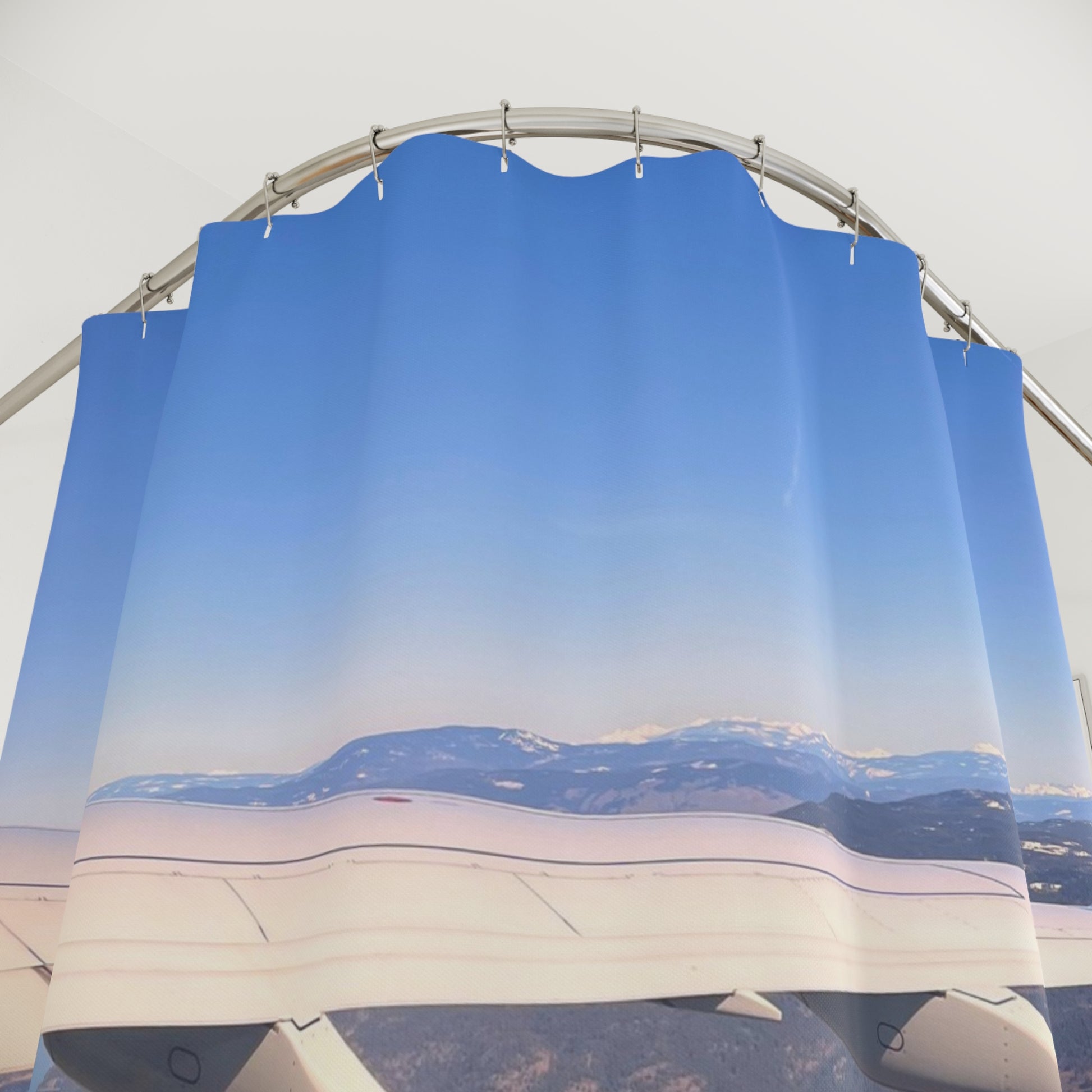 Aerial view of airplane wing flying above snow-capped mountains under a vast, clear blue sky with horizon in the distance.