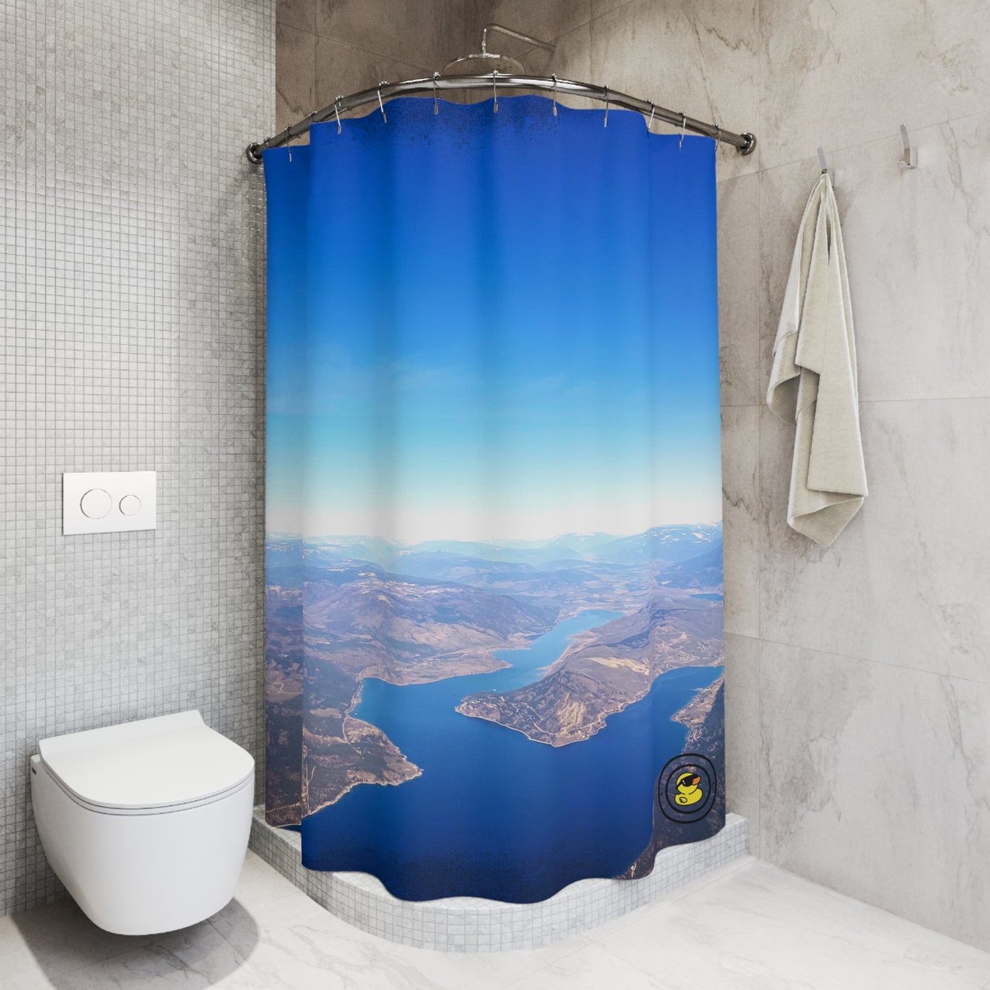 Modern bathroom with blue aerial landscape shower curtain, wall-mounted towel, and sleek toilet design.