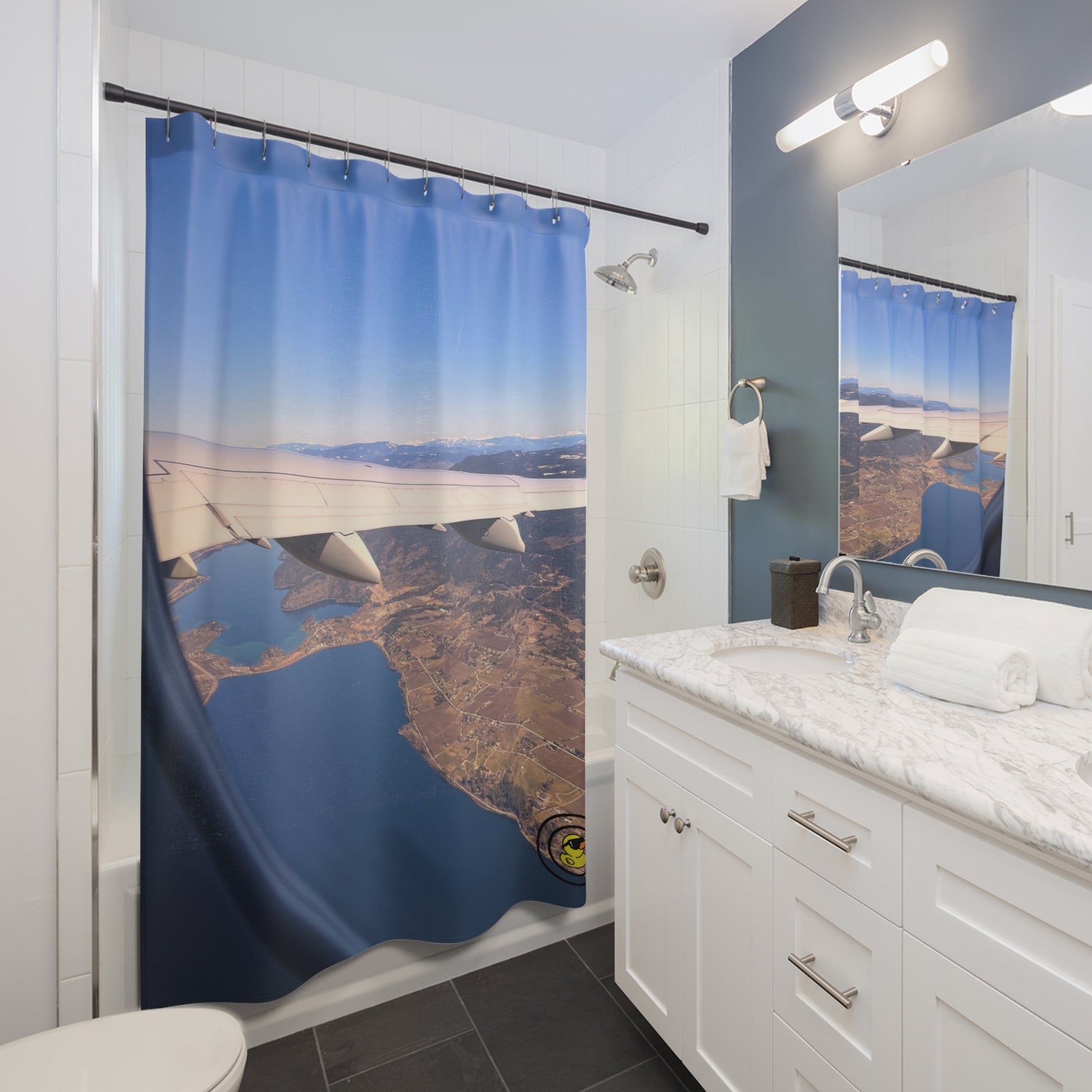 Modern bathroom with a shower curtain featuring an aerial view of coastline and airplane wing over blue ocean.