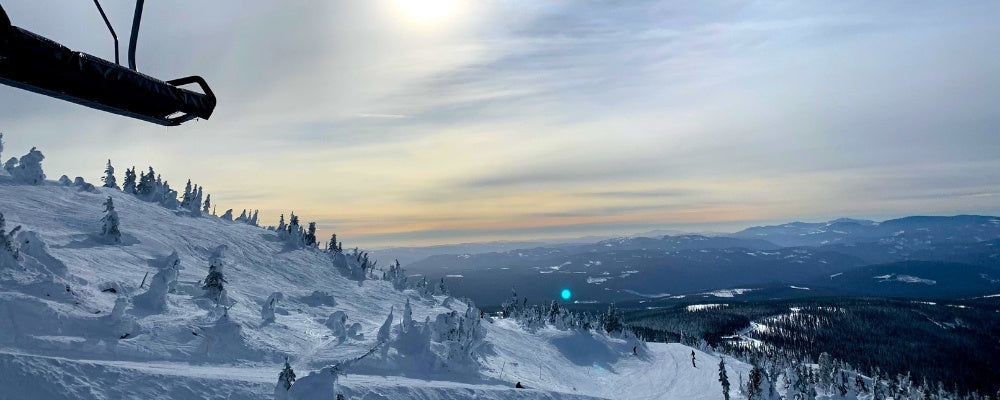 Ski chairlift gliding above snow-covered trees at sunrise, with expansive mountain views and soft morning light.