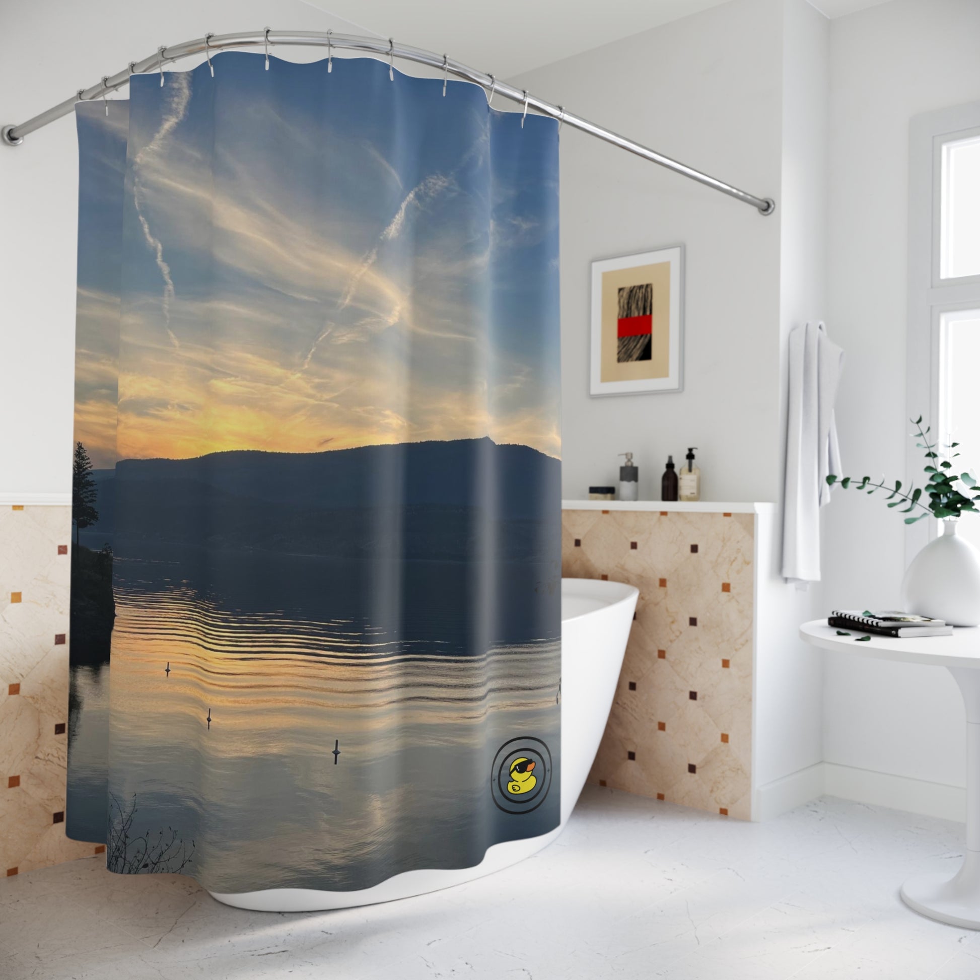 Shower curtain with a peaceful lake sunset scene. In a modern white bathroom with tub and wall art.
